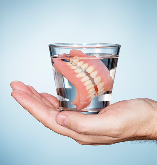 Hand holding a water glass with dentures
