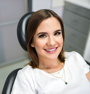 Woman in white shirt smiling while sitting in dental chair