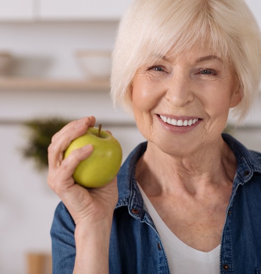 Woman eating a green apple after replacing missing teeth with dental implants