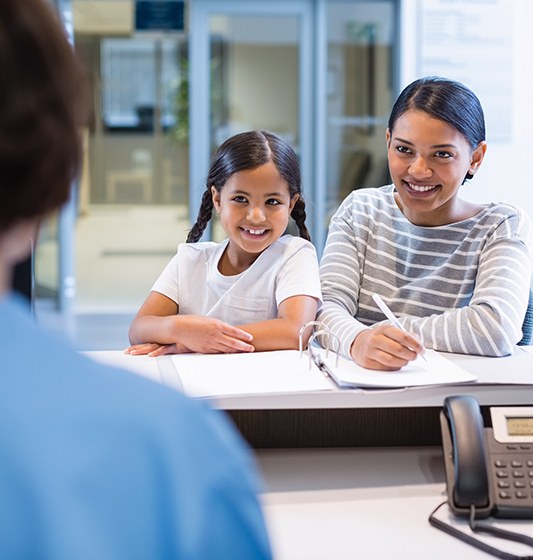 Mother and daughter completing dental insurance forms at reception desk