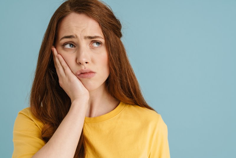 A woman needing emergency dentistry holding her jaw