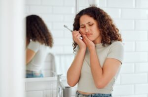 Girl holding jaw in pain while brushing teeth.